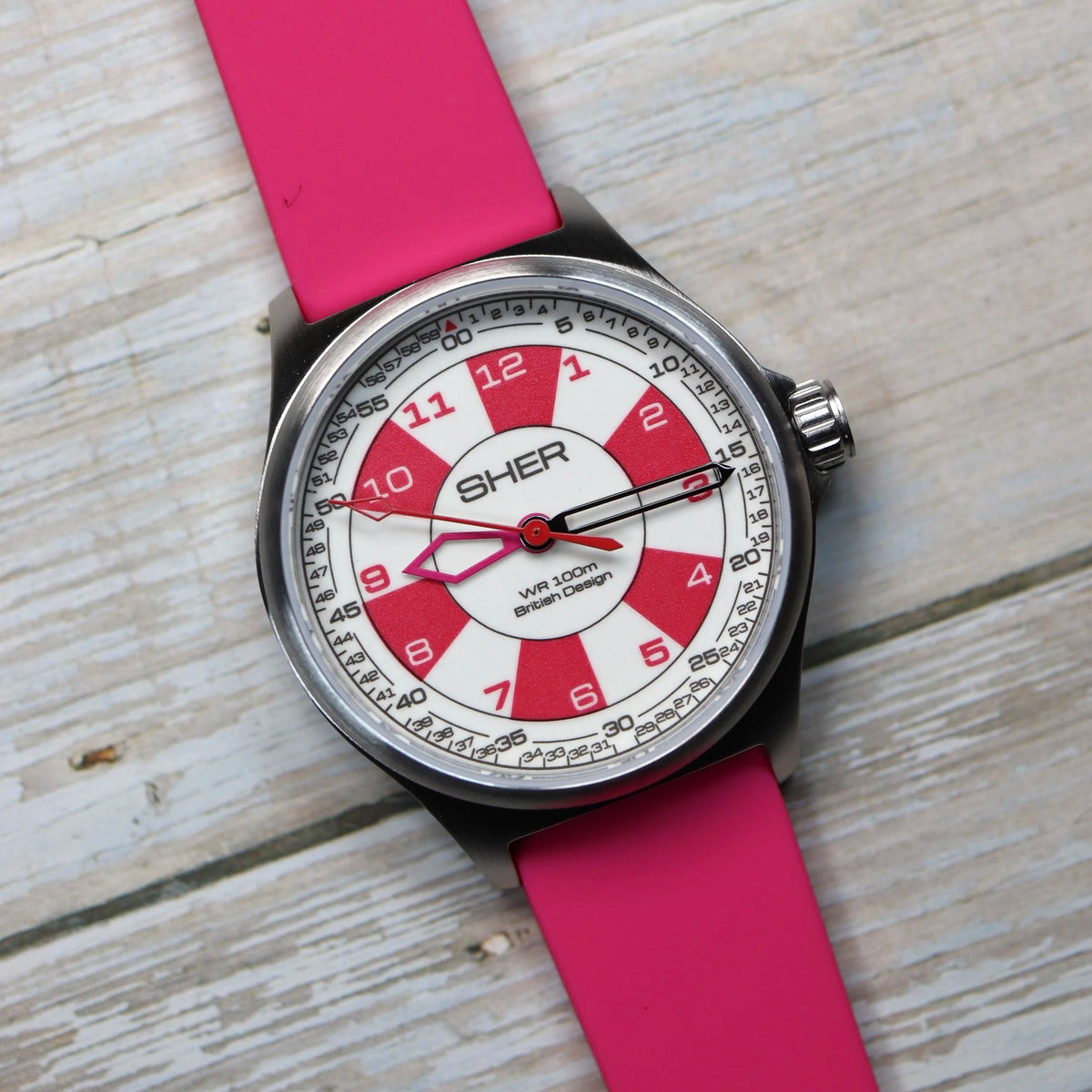 Watch with a pink strap and red face on a wooden surface